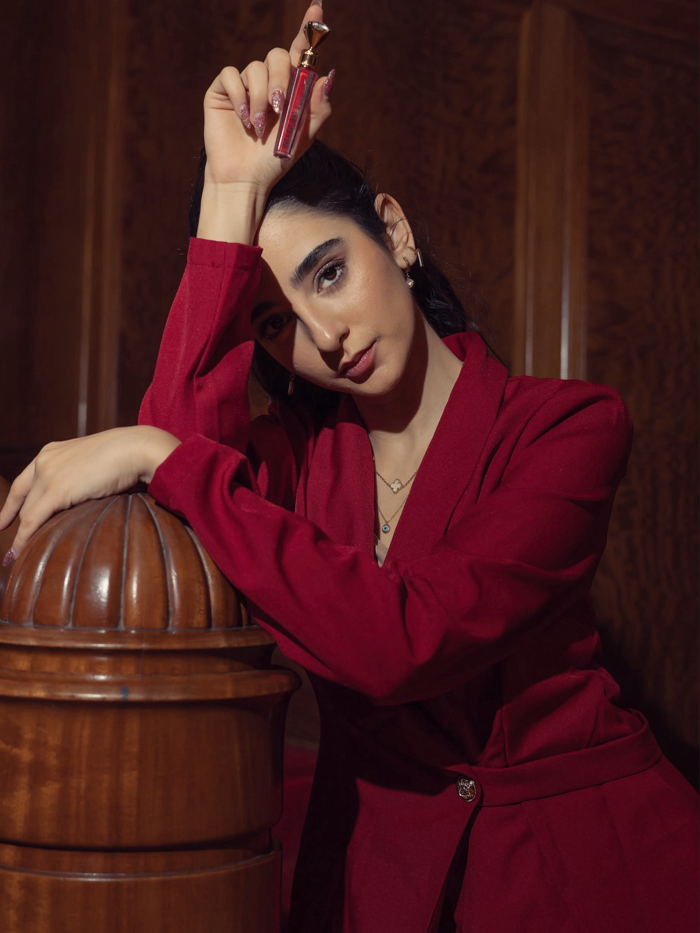 Model in a red blazer holding a lip gloss product